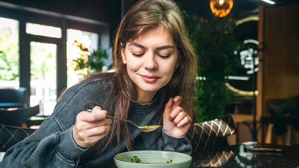 mujer comiendo sopa de verduras en una cafetería