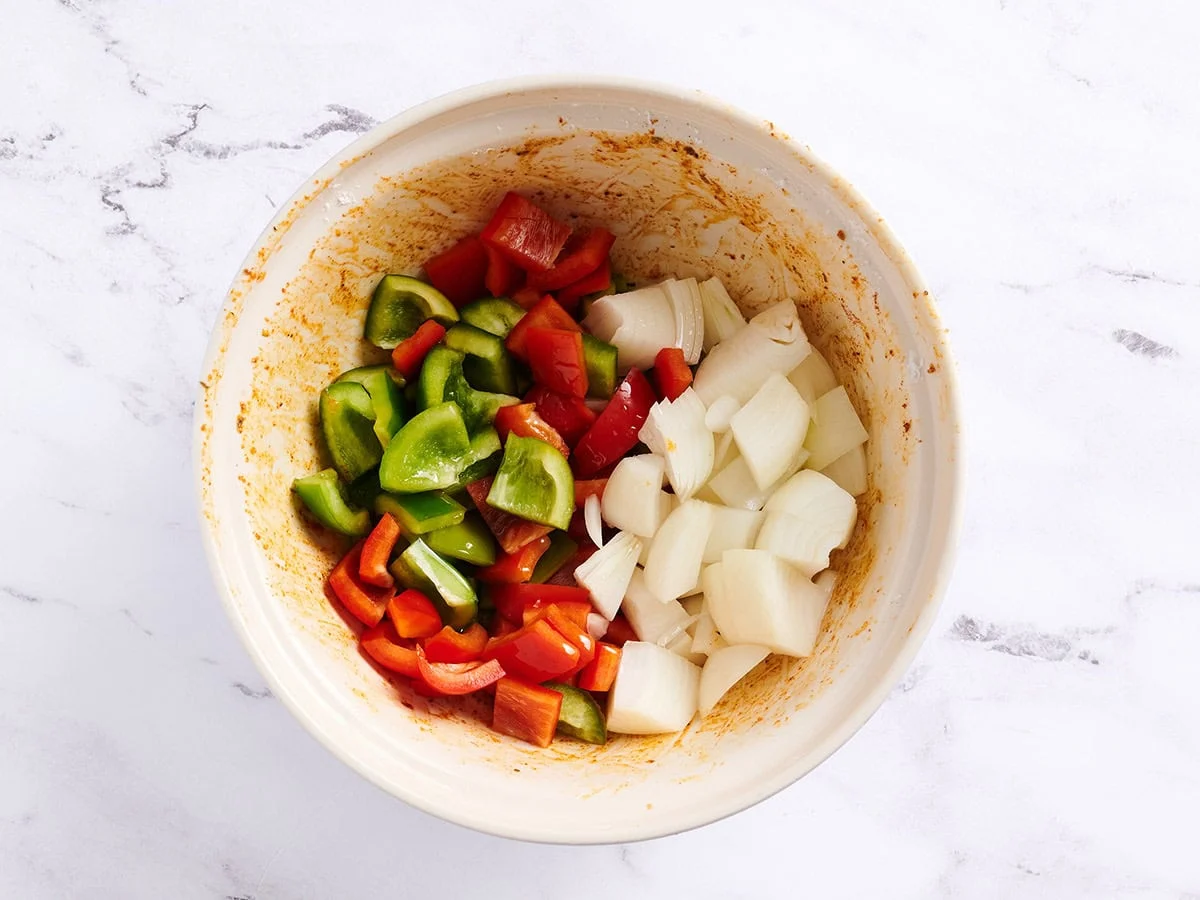 Pimientos morrones y cebolla en un bol blanco con el condimento cajún.