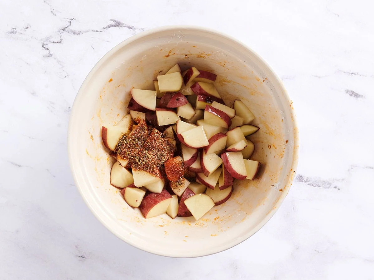 Patatas en cubos con condimento cajún en un recipiente blanco.