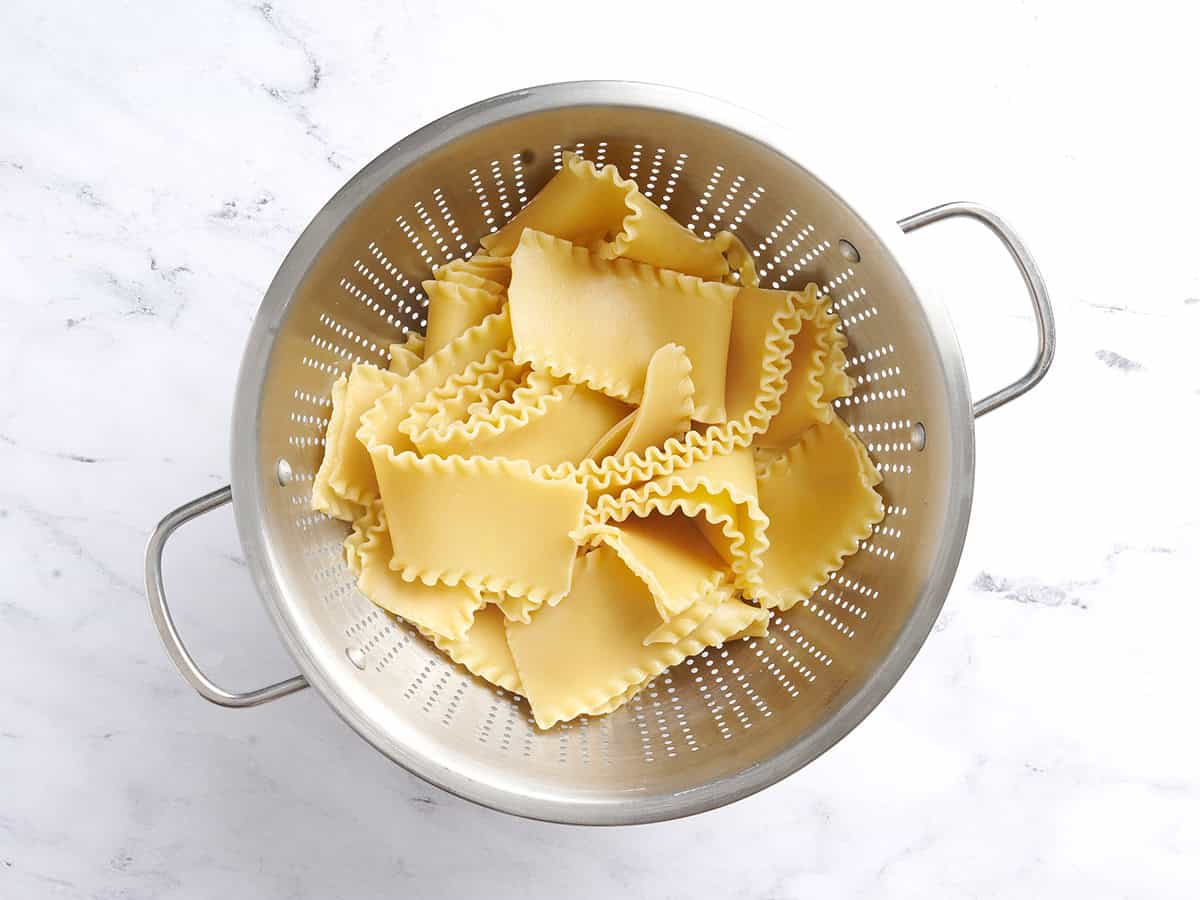 Fideos de lasaña cocidos en un colador.