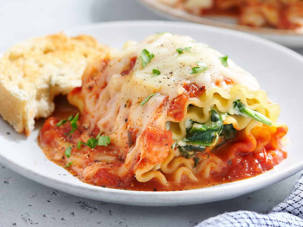 Vista lateral de una lasaña de espinacas y ricotta enrollada en un plato con pan.