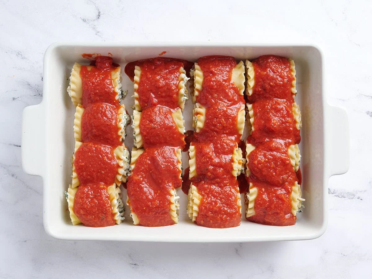 Lasaña se enrolla en una fuente para horno cubierta con salsa.