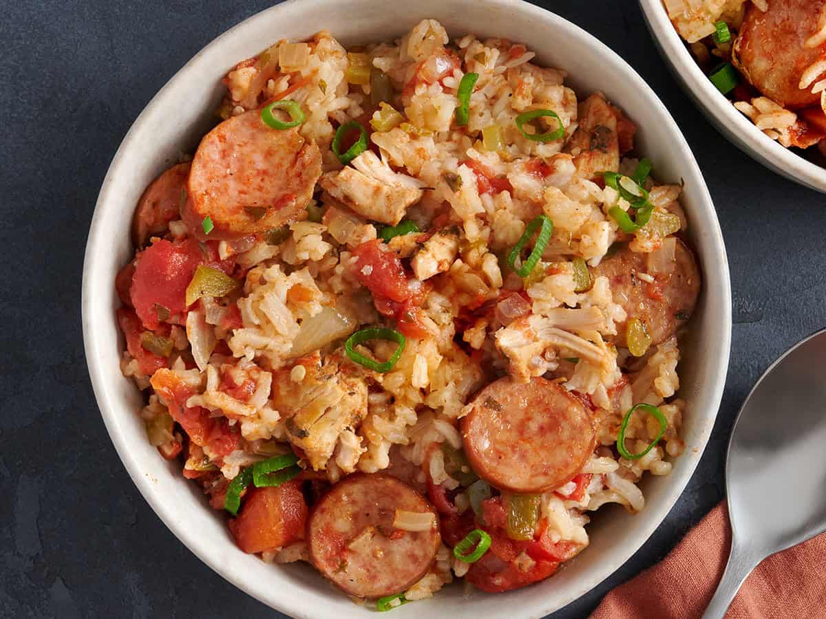 Tazón de jambalaya de cocción lenta adornado con cebollas verdes en un tazón blanco con una cuchara. 