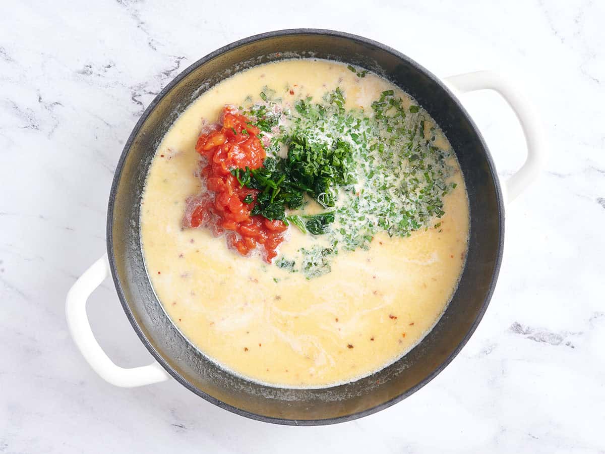 Se añaden tomates, espinacas, hierbas y parm a la salsa para casarme con albóndigas en una sartén.