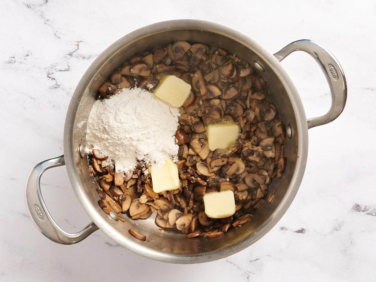 Se añade mantequilla y harina a una sartén de champiñones salteados.