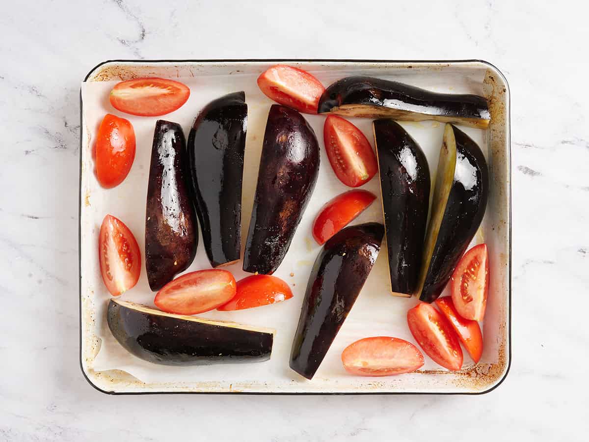 Cuartos de berenjena y tomate asados en una bandeja para horno.