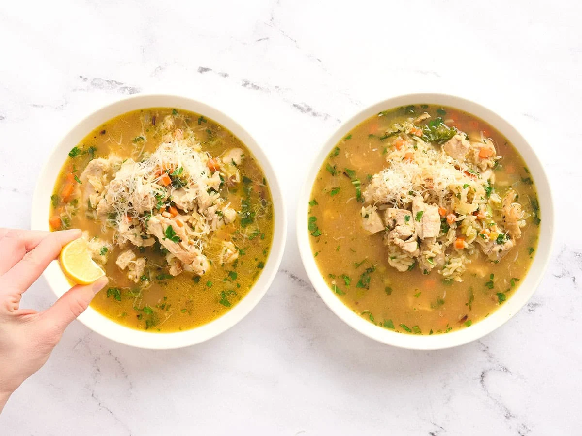 Dos tazones de arroz caldoso con una mano exprimiendo limón sobre uno.