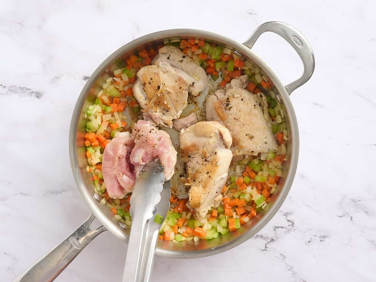 Muslos de pollo cocidos en una sartén con mirepoix.