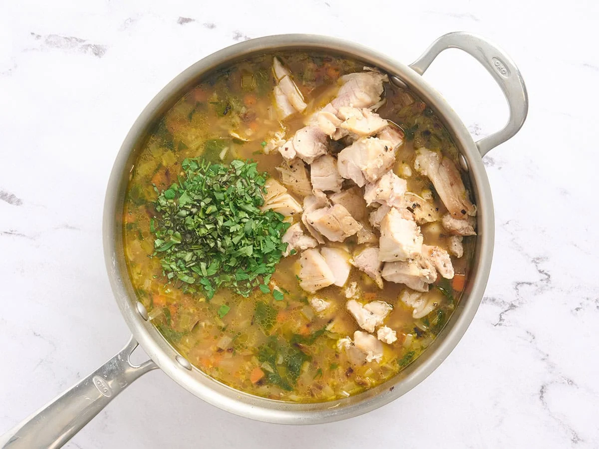 Hierbas frescas y pollo cortado en cubitos agregados a una olla de arroz caldoso.