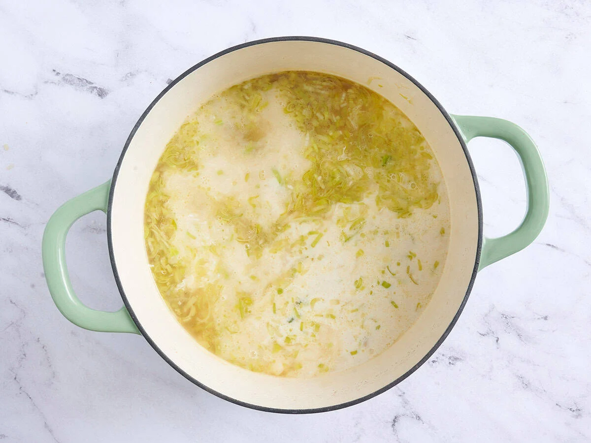 Crema templada agregada a la sopa de papa y puerro en una olla.