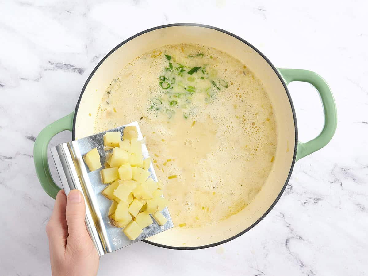 Se añaden patatas cortadas en cubitos y cebollas verdes a una olla de sopa de patatas y puerros.