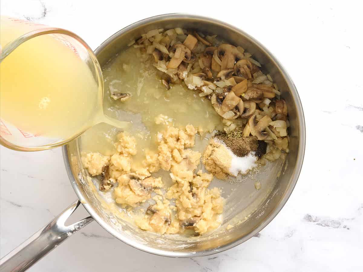 Caldo añadido a un roux y champiñones en una sartén.