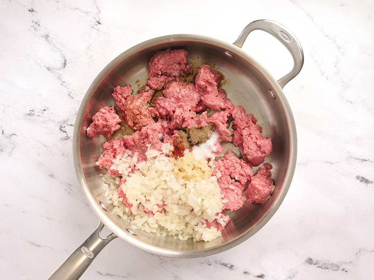 Cebolla picada, carne molida y especias en una sartén.
