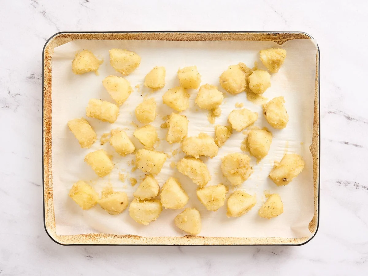 Patatas en una bandeja para hornear forrada con papel pergamino.