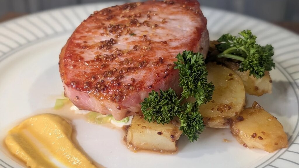 Chuleta de tocino glaseado asado de Trisha con col rizada estofada, salsa de crema de mostaza y patatas baby con mantequilla
