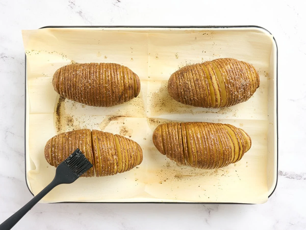 Patatas Hasselback untadas con aceite sazonado a mitad de cocción.