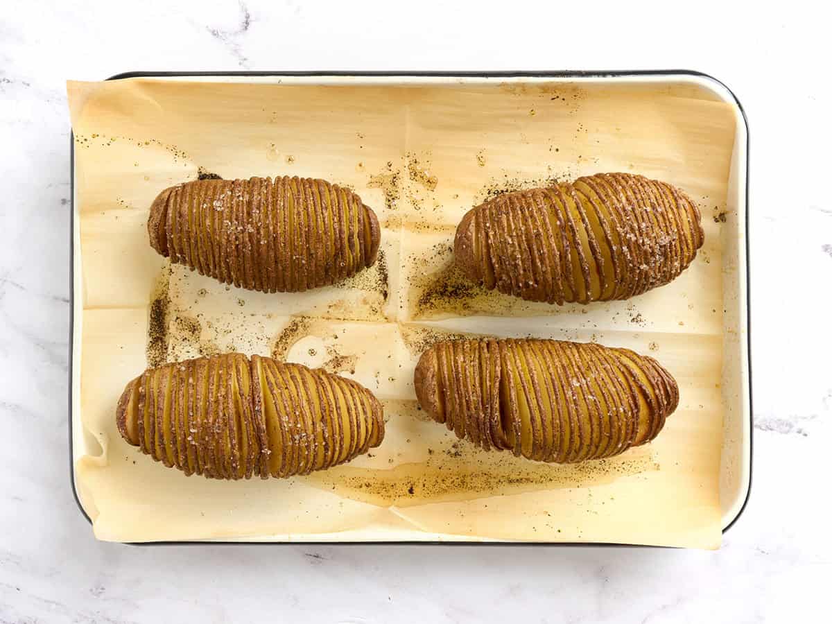 Patatas Hasselback en una bandeja para hornear forrada con papel pergamino.