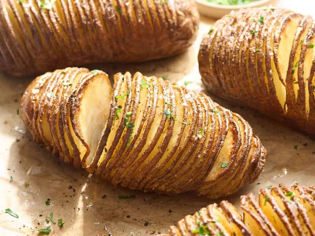 Side view of hasselback potatoes on parchment paper.