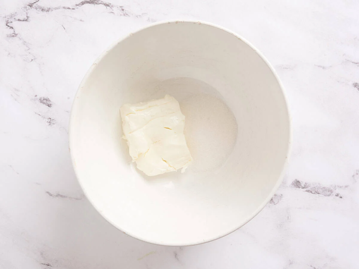 Se agrega azúcar y queso crema a un tazón para mezclar.
