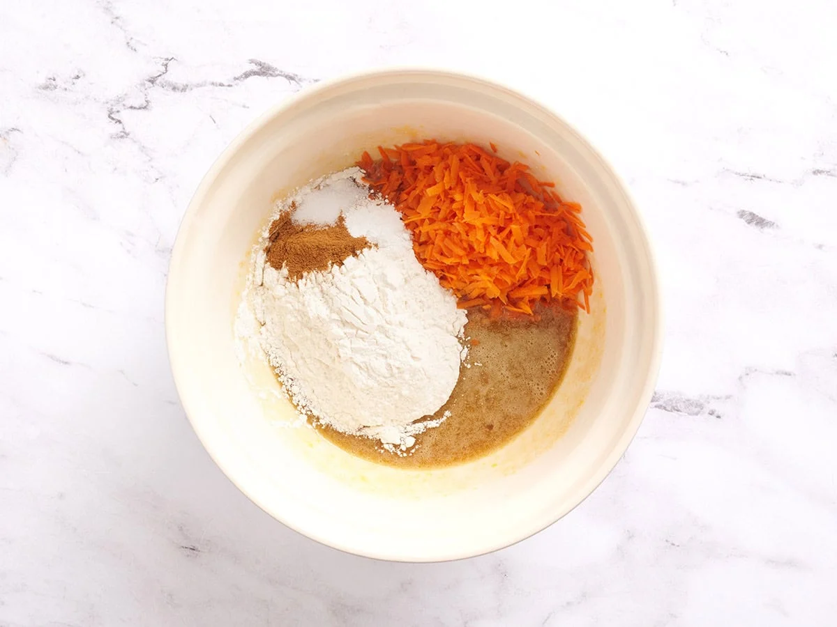 Harina, especias, zanahorias ralladas y masa para pastel en un bol.