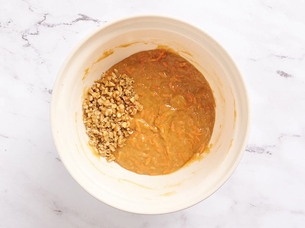 Se agregan nueces a la masa de la barra de pastel de zanahoria en un tazón.