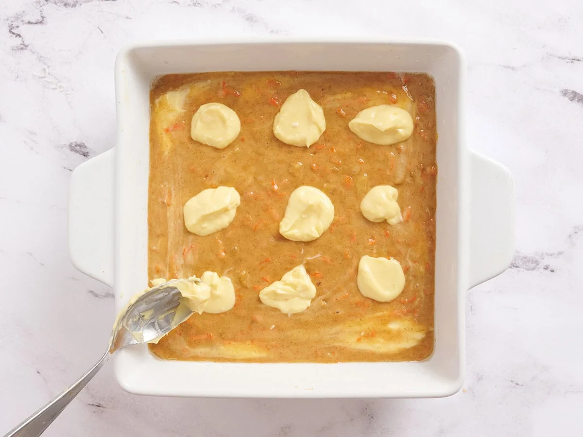 Se añaden cucharadas de tarta de queso a la masa para las barras de pastel de zanahoria.
