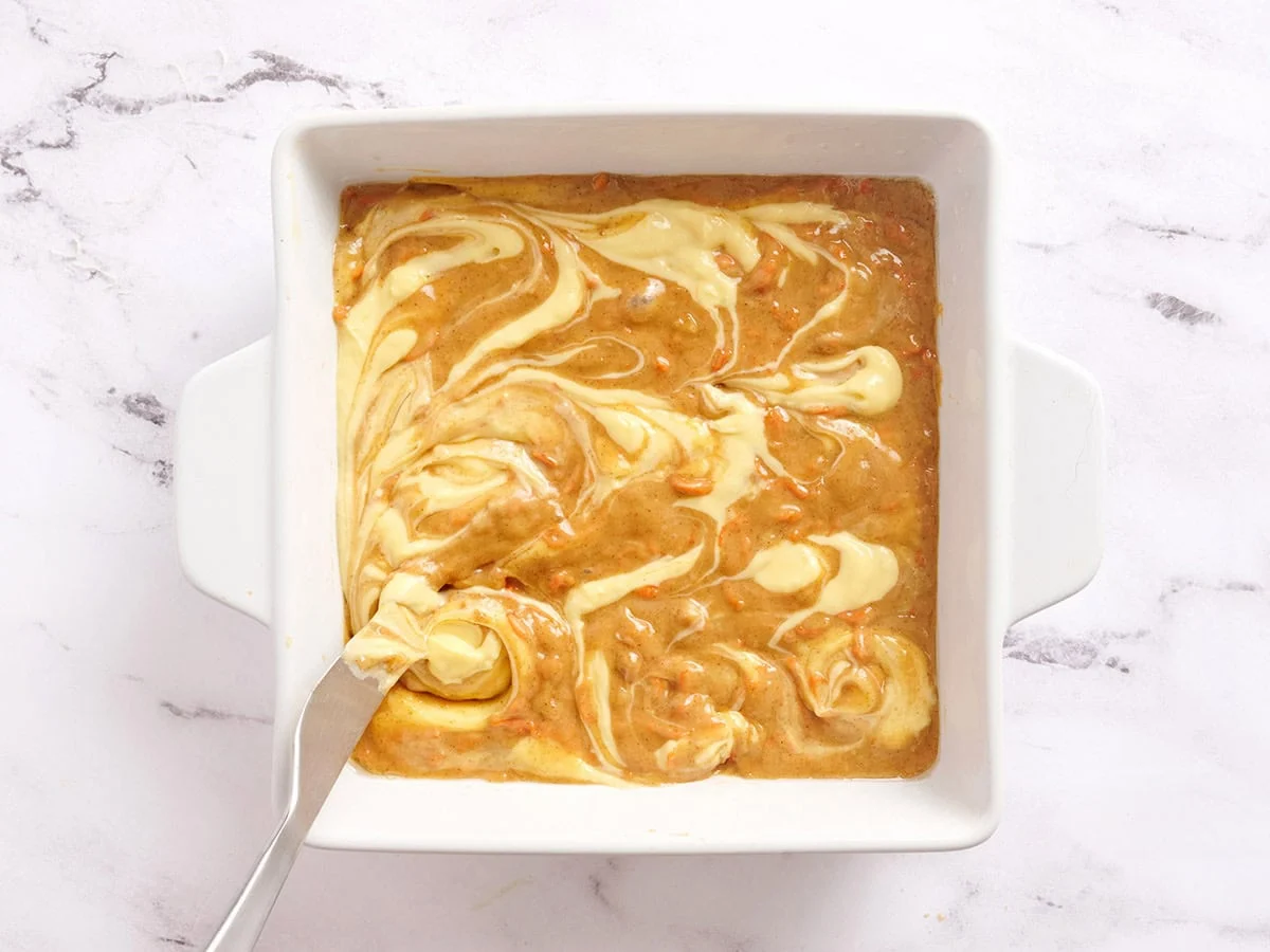 La tarta de queso se arremolina sobre barras de pastel de zanahoria en una fuente para horno.