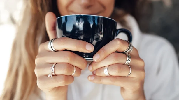 Primer plano de la mano de una mujer sosteniendo una taza de café y usando anillos de plata