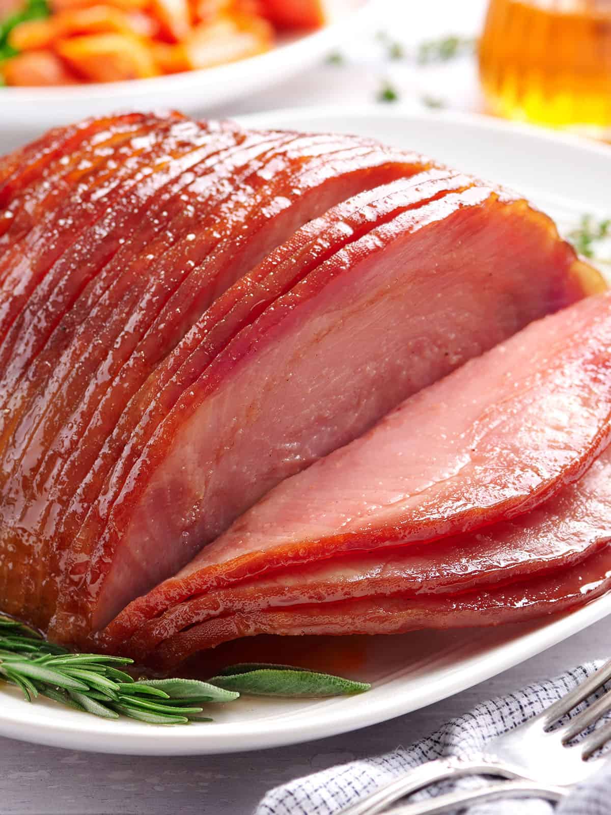 Vista lateral de jamón glaseado con miel en rodajas en un plato con hierbas.