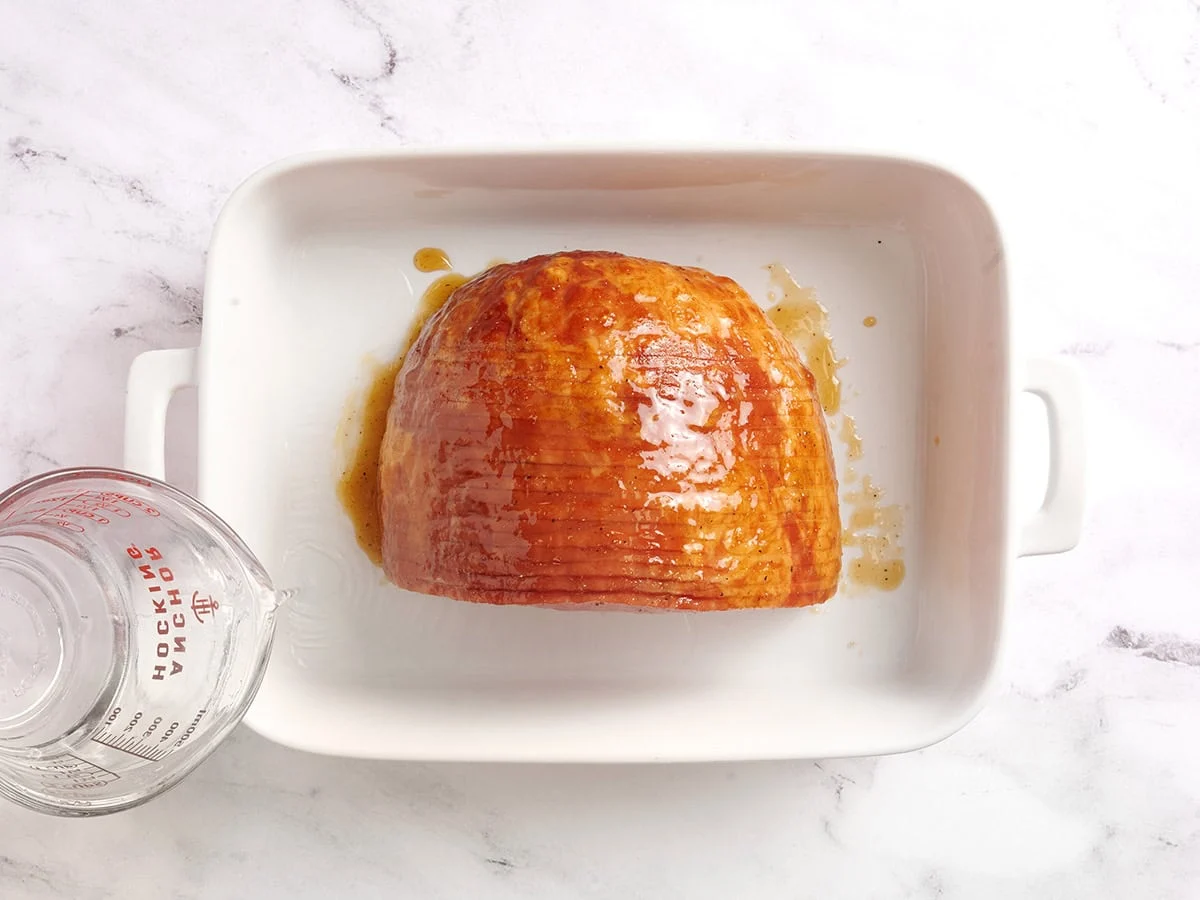 Se vierte agua en una fuente para horno con jamón glaseado con miel.
