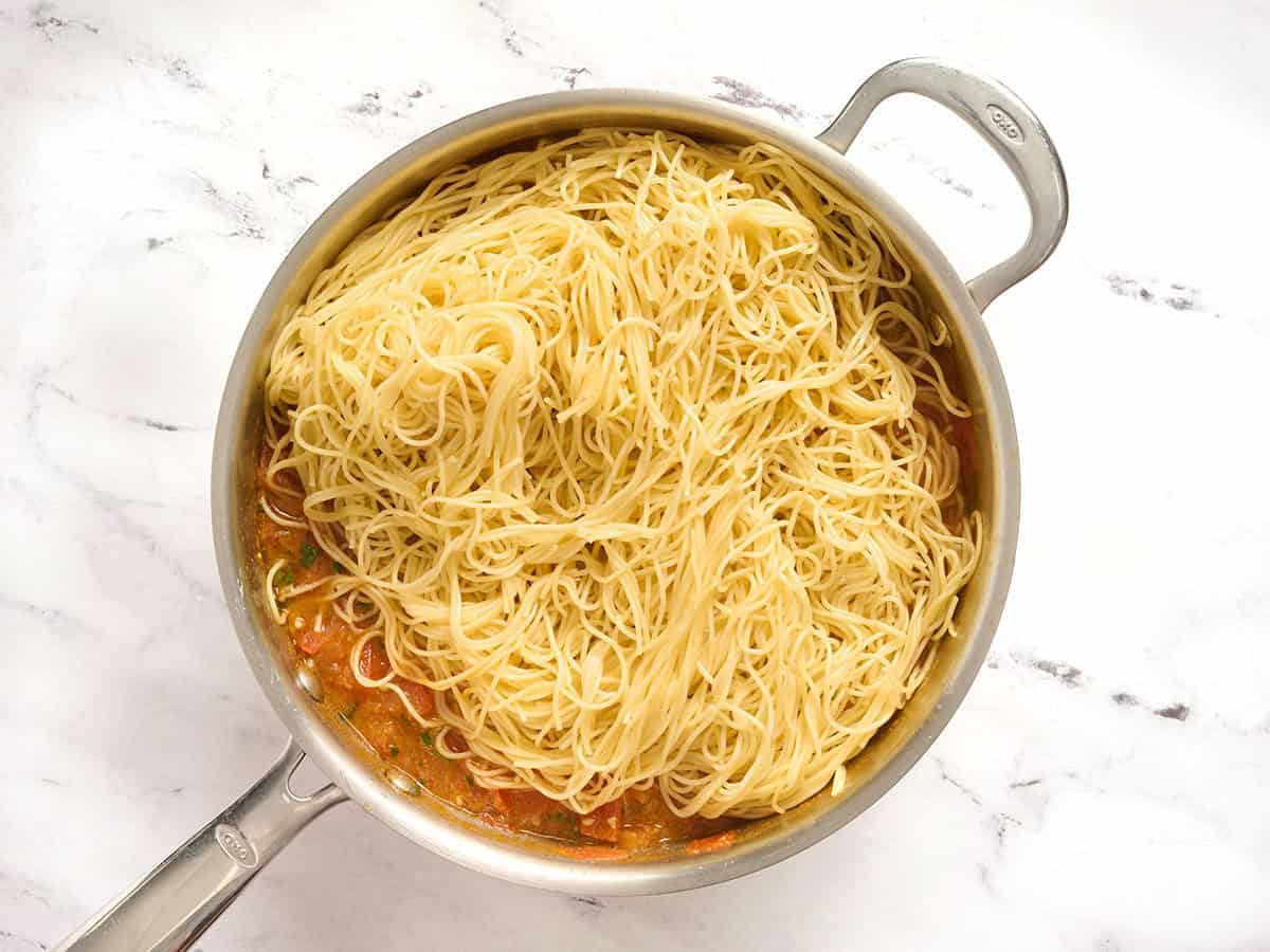 Pasta cabello de ángel agregada a una sartén con verduras.