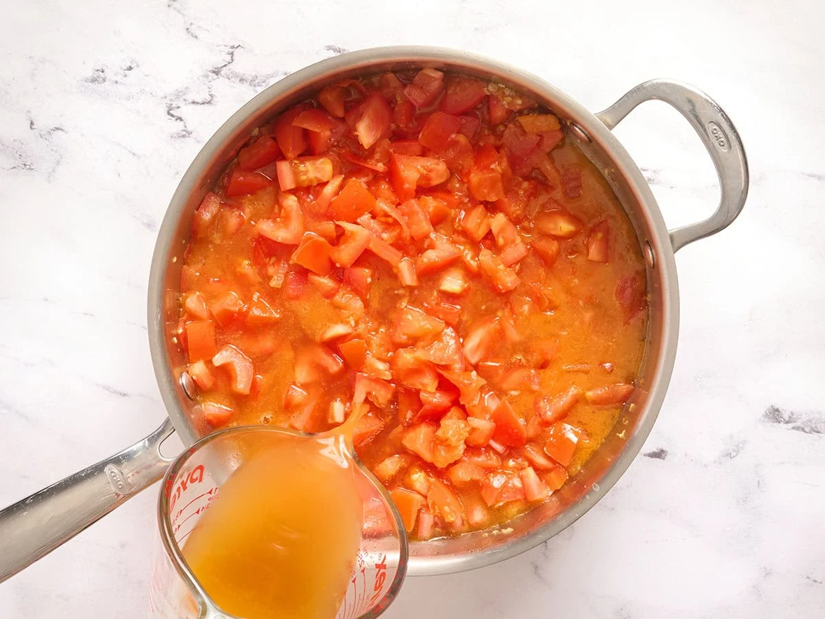 Se agrega caldo a los tomates en una sartén.
