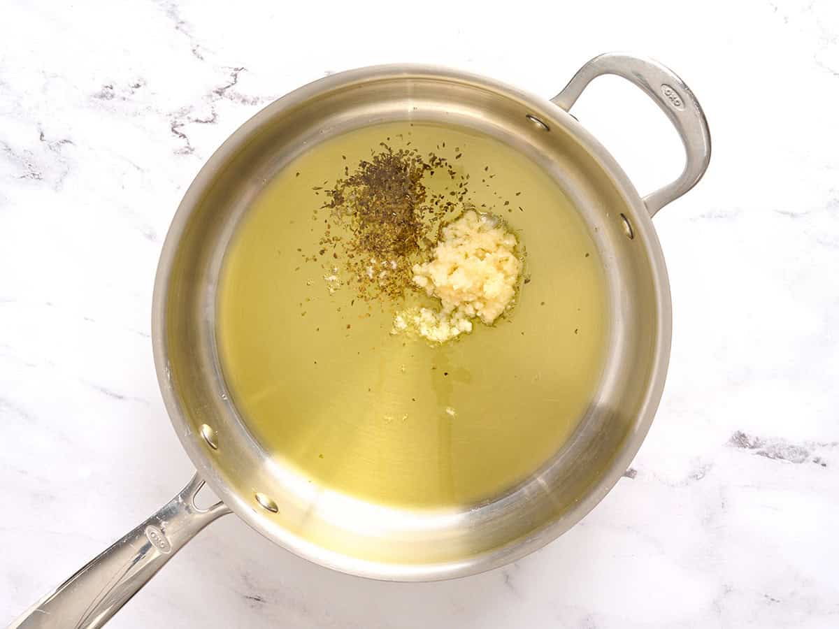 Ajo, hierbas y aceite en una sartén.