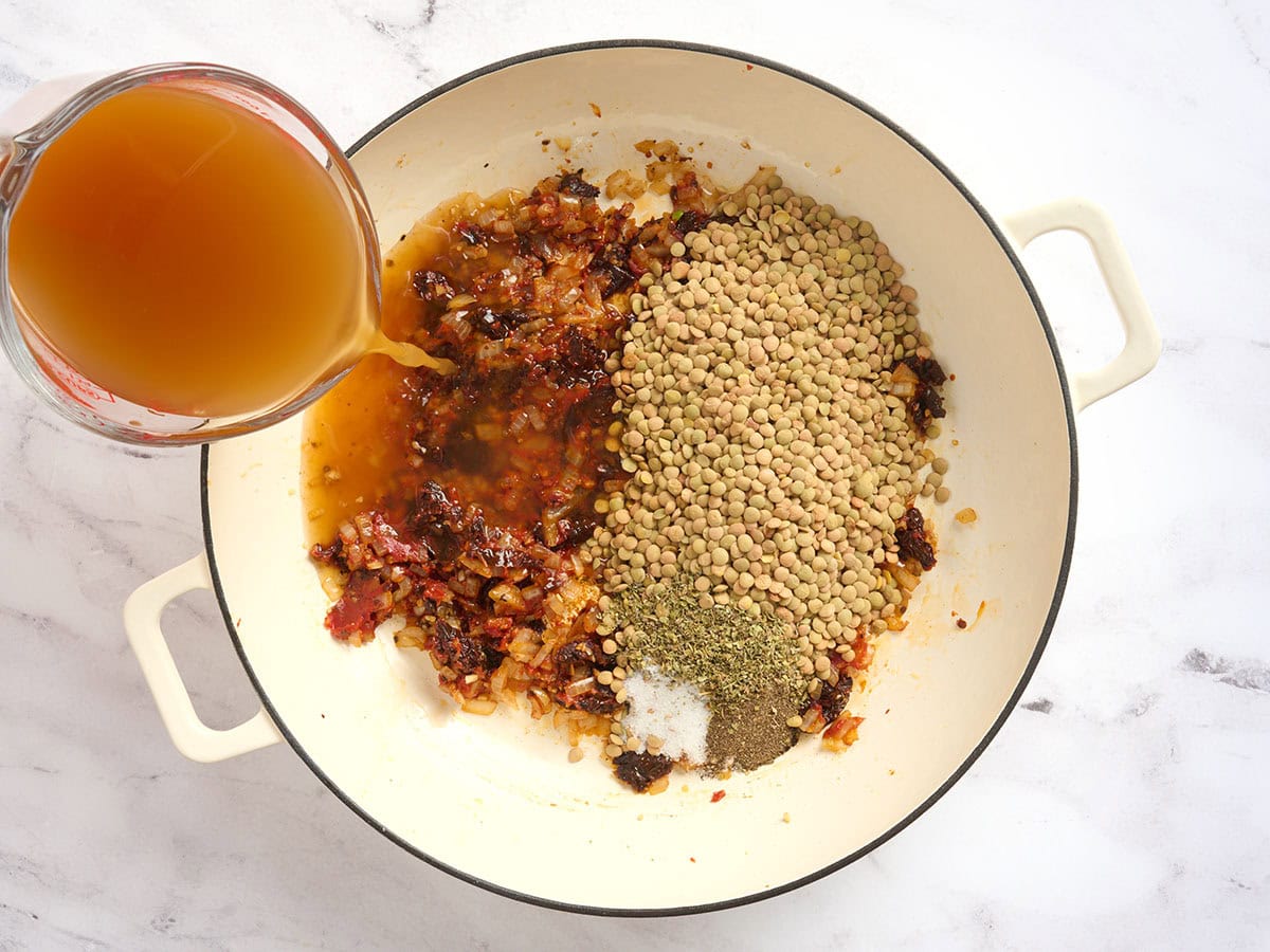 Caldo y lentejas secas agregadas a una olla con tomates secos.