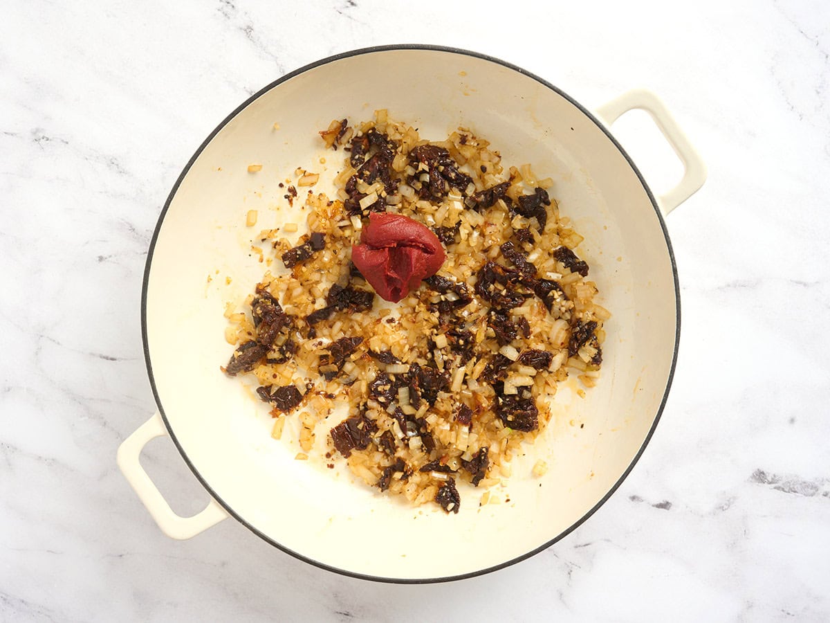Cebollas y ajos salteados en una olla con tomates secos y pasta de tomate.