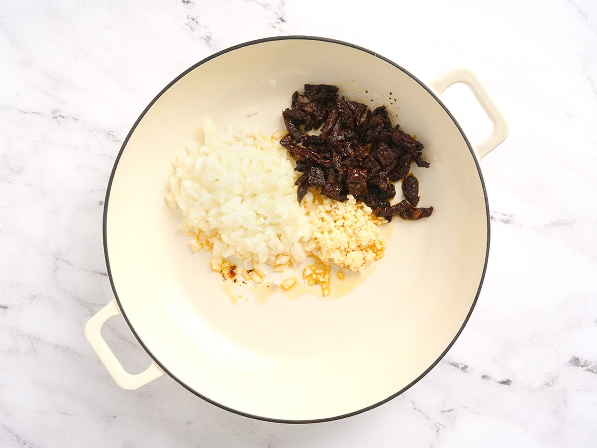 Ajo picado, cebolla picada y tomates secos picados en una olla.