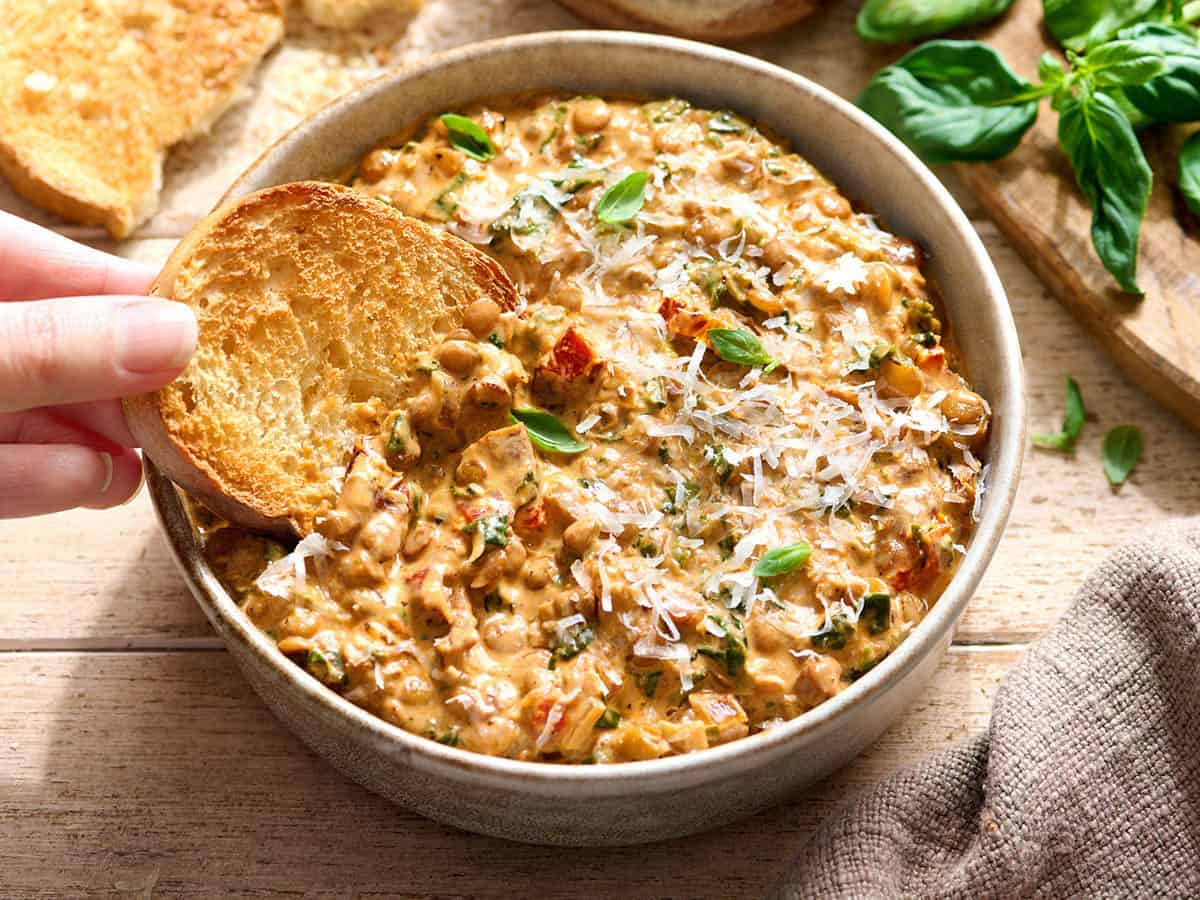 Una mano mojando una rebanada de pan tostado en un plato de lentejas cásate conmigo.