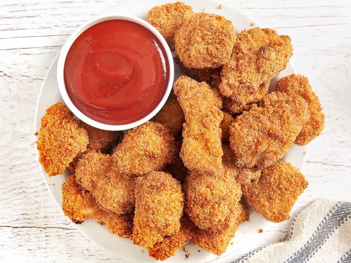 Vista aérea de nuggets de pollo al horno en un plato con una olla de salsa de tomate.