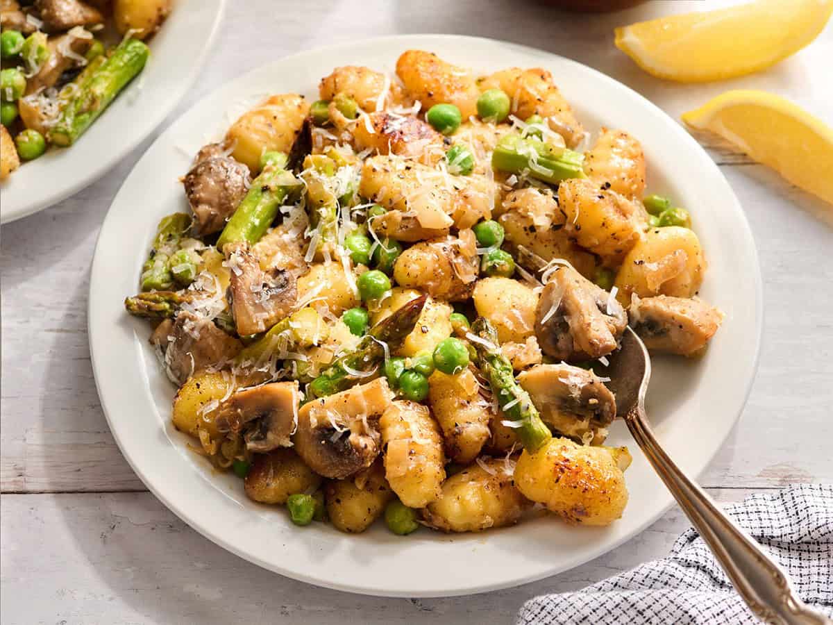 Un plato de ñoquis de verduras de primavera en un plato con un tenedor.