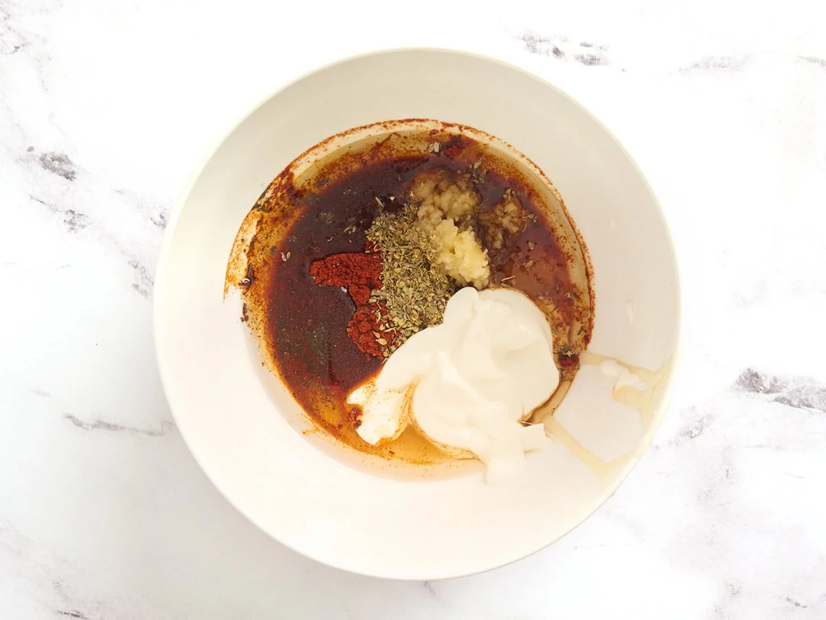 Aceite, yogur, ajo y condimentos en un bol.