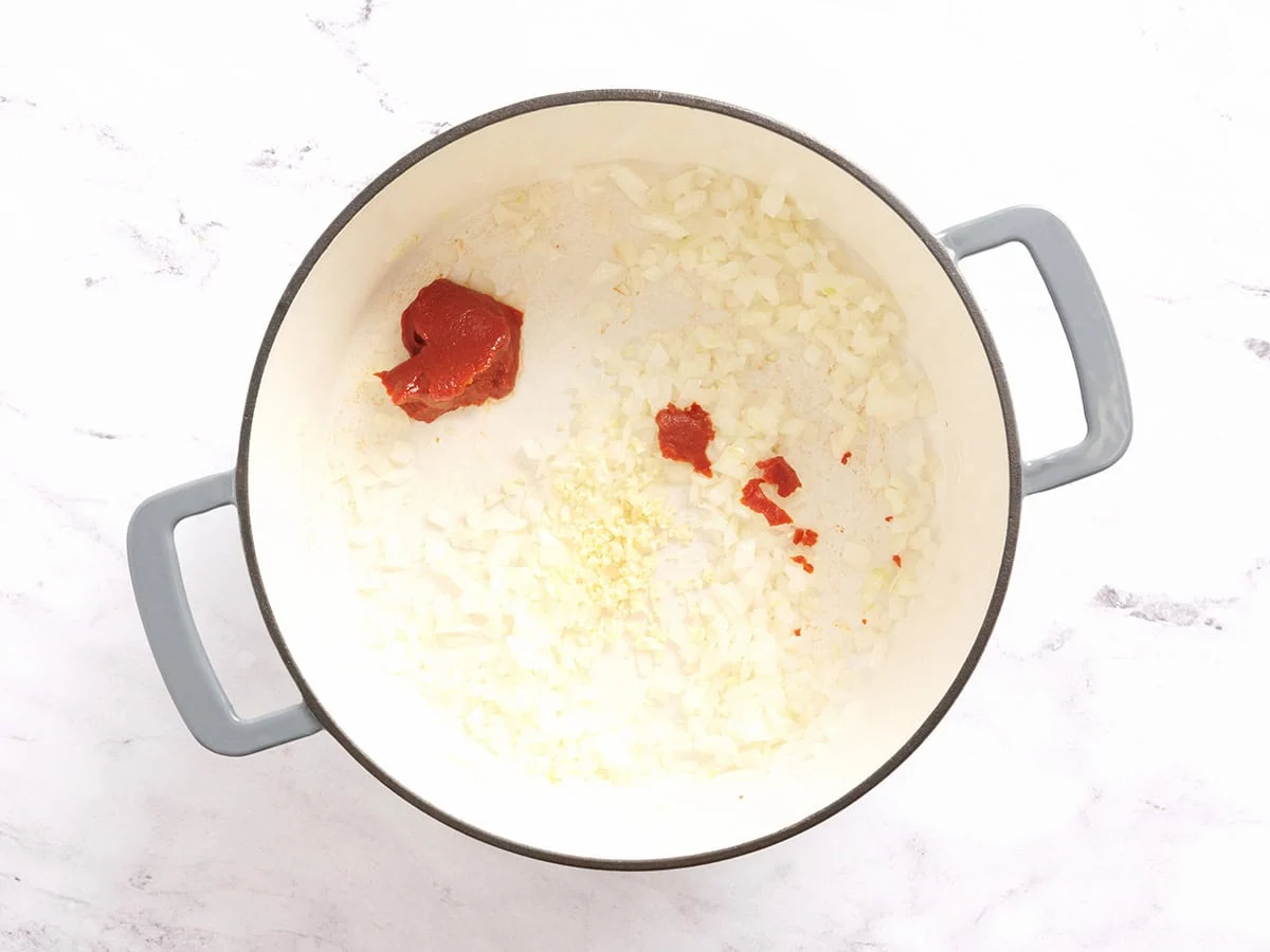Se agrega pasta de tomate y ajo picado a la cebolla salteada en una olla.