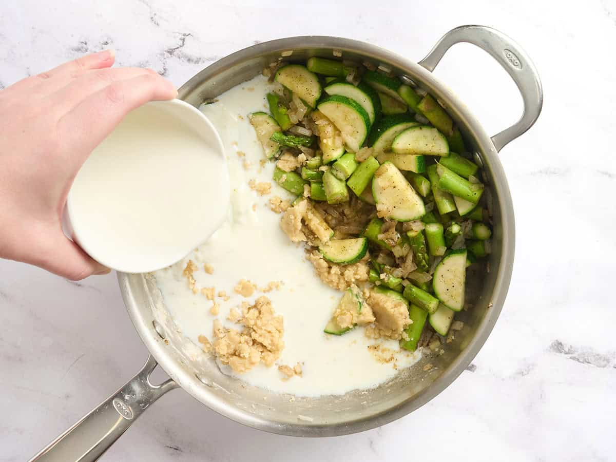 Leche agregada a una sartén de verduras salteadas.