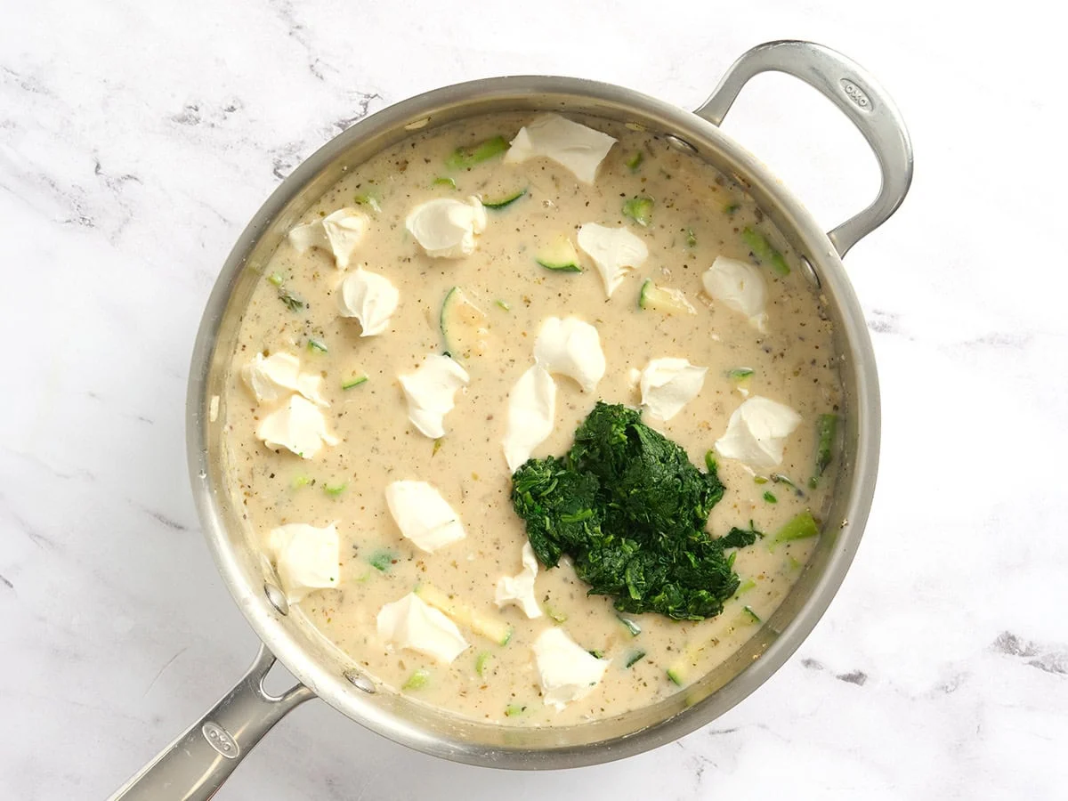 Se agregan cubos de queso crema y espinacas descongeladas a una sartén con salsa cremosa y verduras.