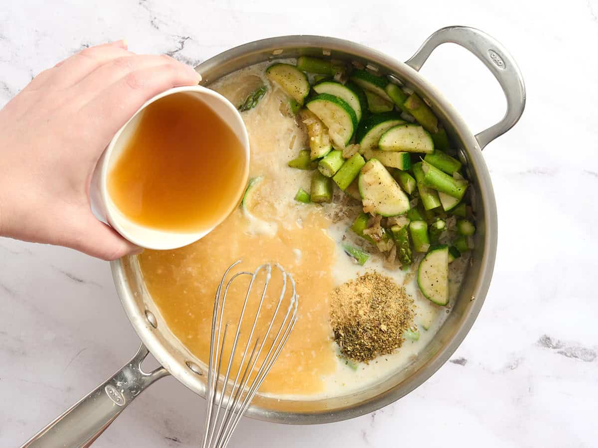 Se agrega caldo a una sartén con verduras tiernas y una salsa de leche espesa.