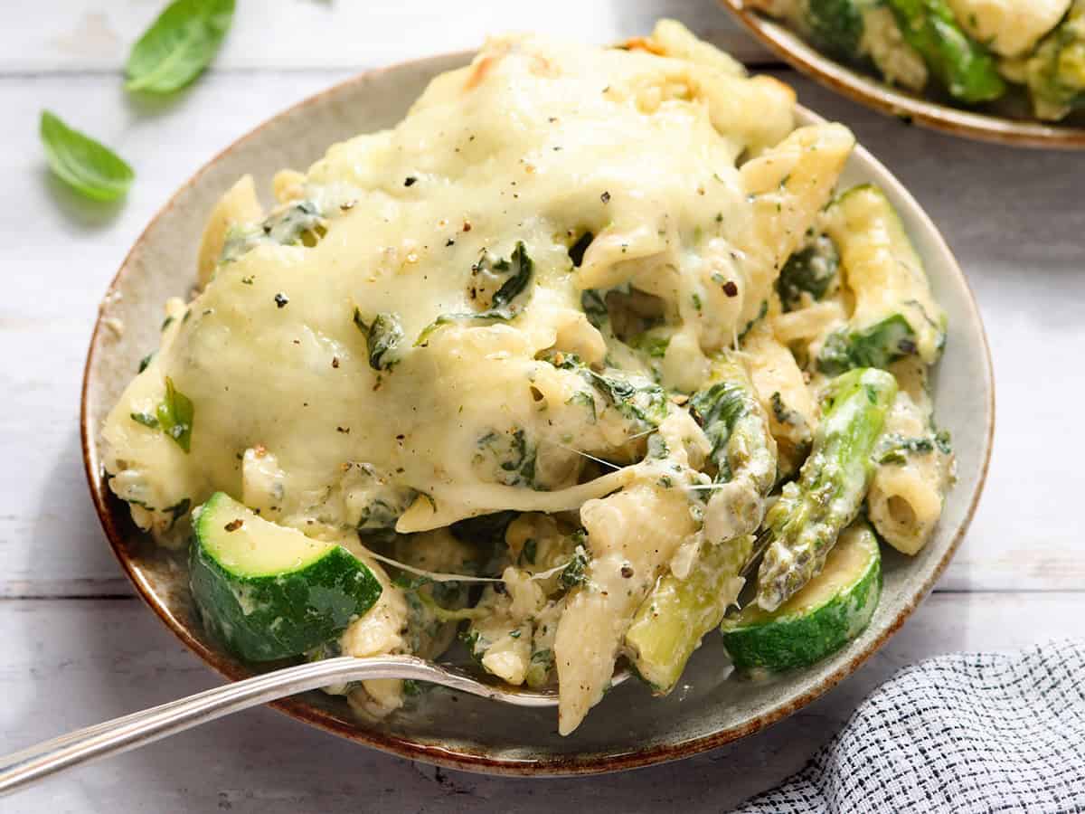 Vista lateral de un plato de pasta al horno con verduras de primavera y un tenedor.