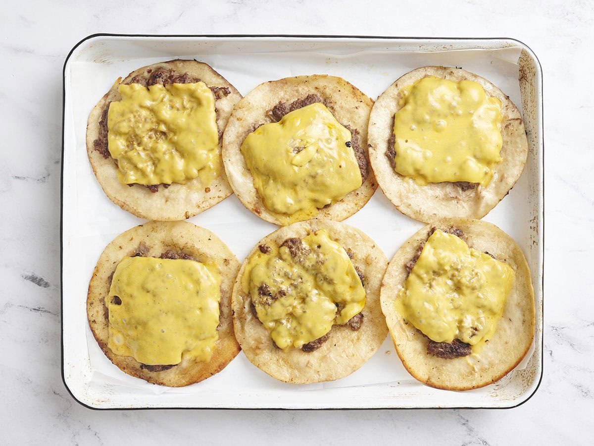 Aplasta los tacos de hamburguesa después de cocinarlos en una bandeja para hornear.