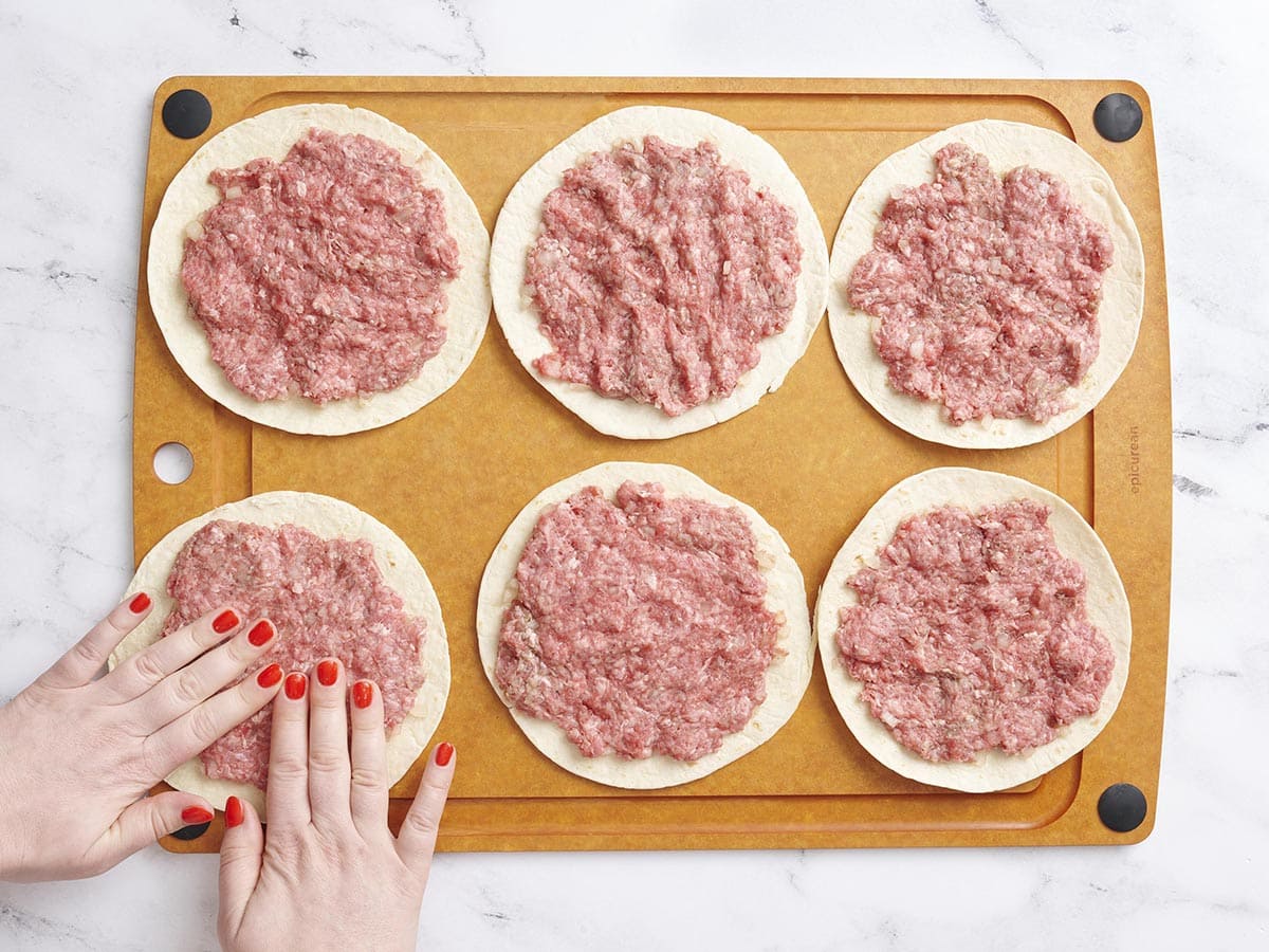 Manos presionando carne molida en tortillas de harina.