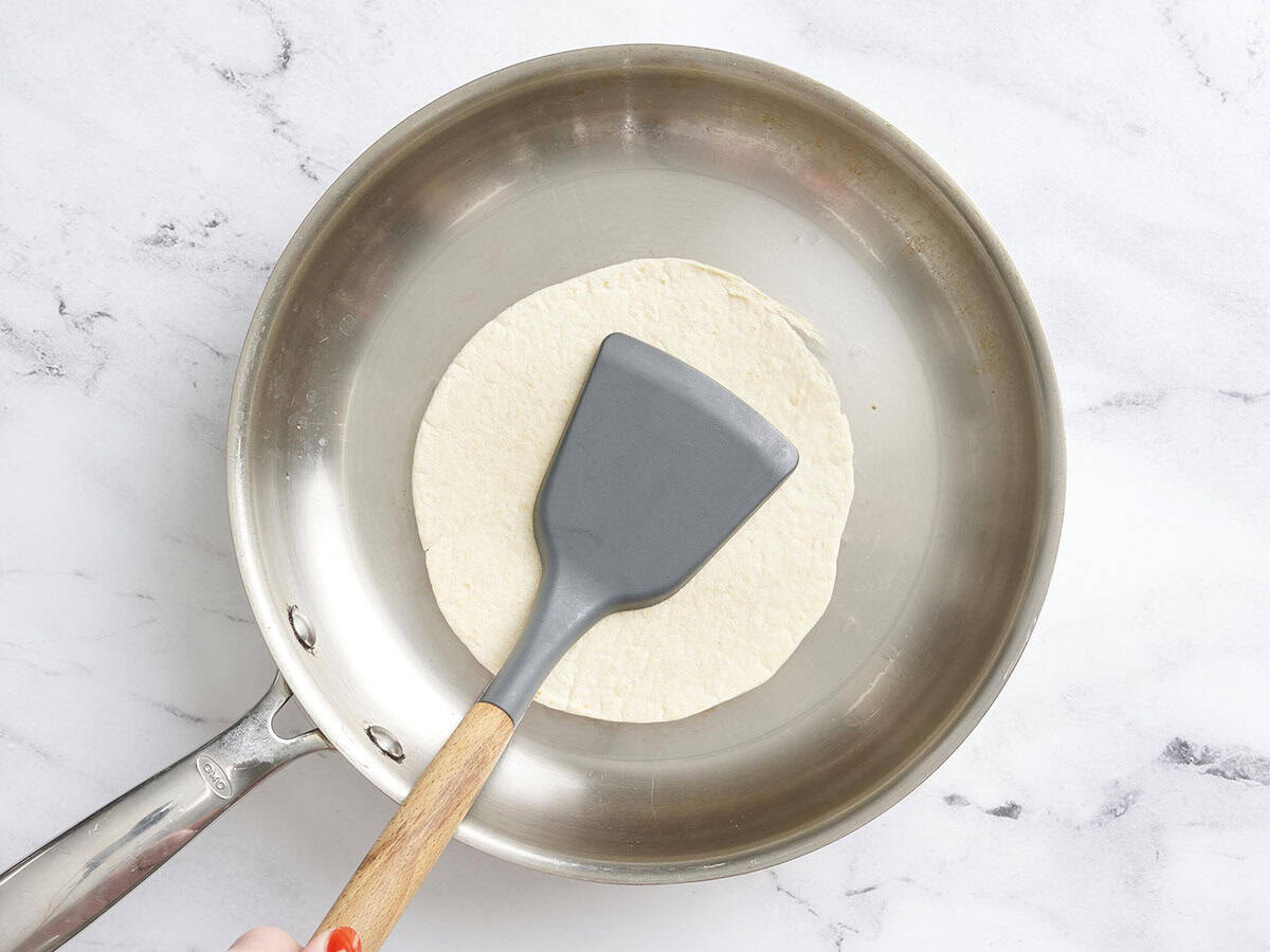 Una espátula presionando una tortilla en una sartén.