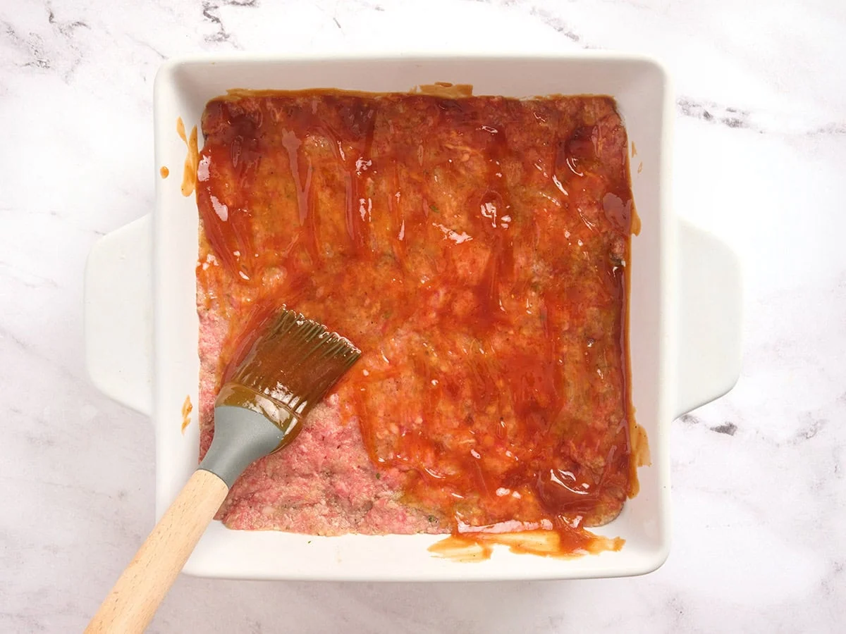 Un glaseado de ketchup se extiende sobre un pastel de carne en una cazuela.