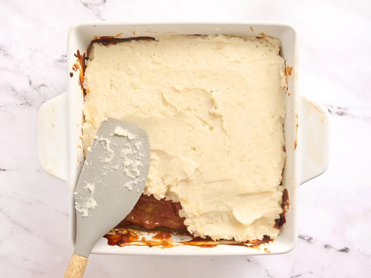 Puré de patatas esparcido sobre una cazuela de pastel de carne en una fuente para horno.